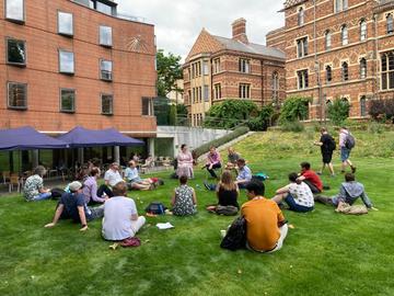 Students at the Digital Humanities @ Oxford Summer School sit on the grass in Keble College, listening to a panel discussion.